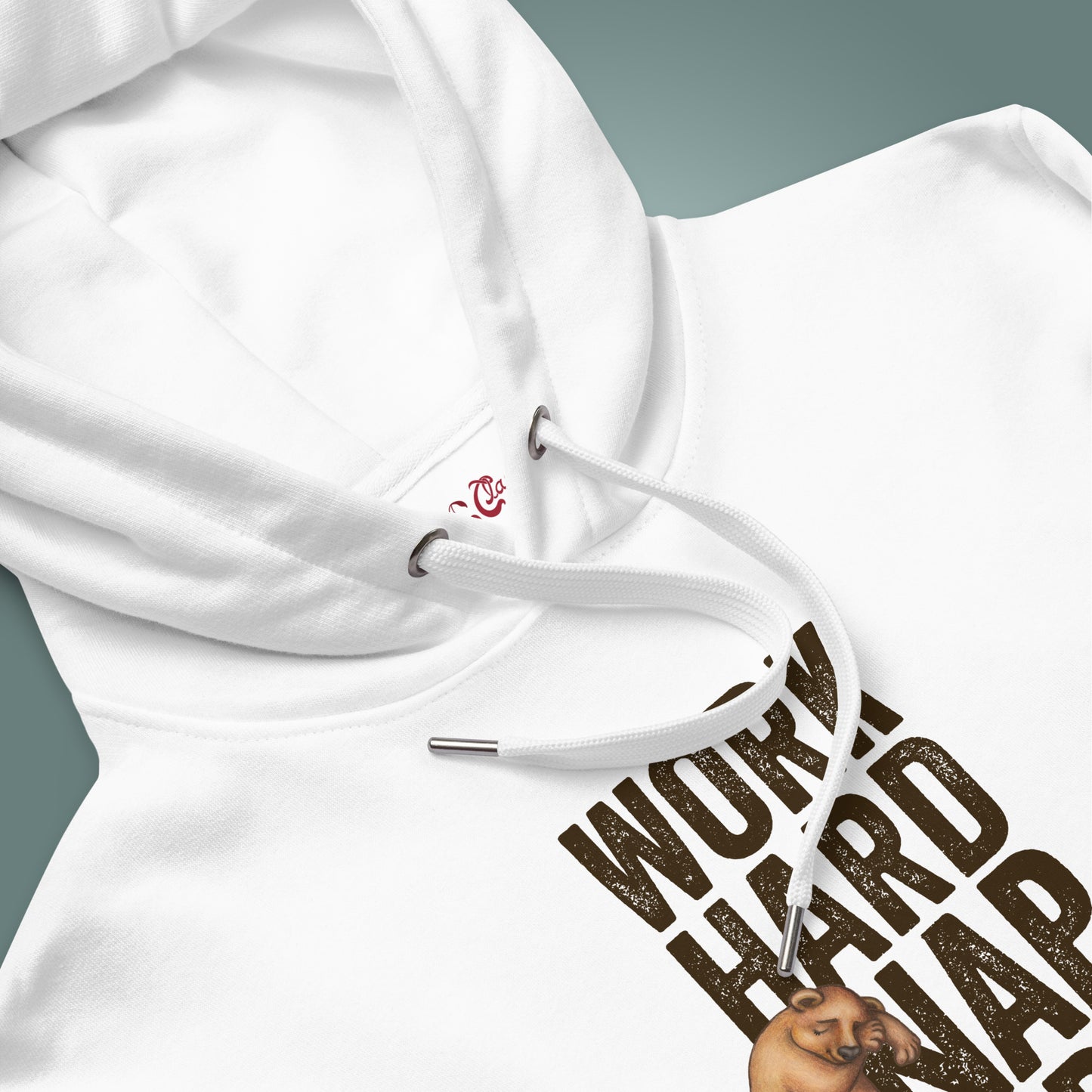 Close up of a white hood with "Work Hard, Nap Hard" design on the body of the sweater below, with the garment showcased on a teal background