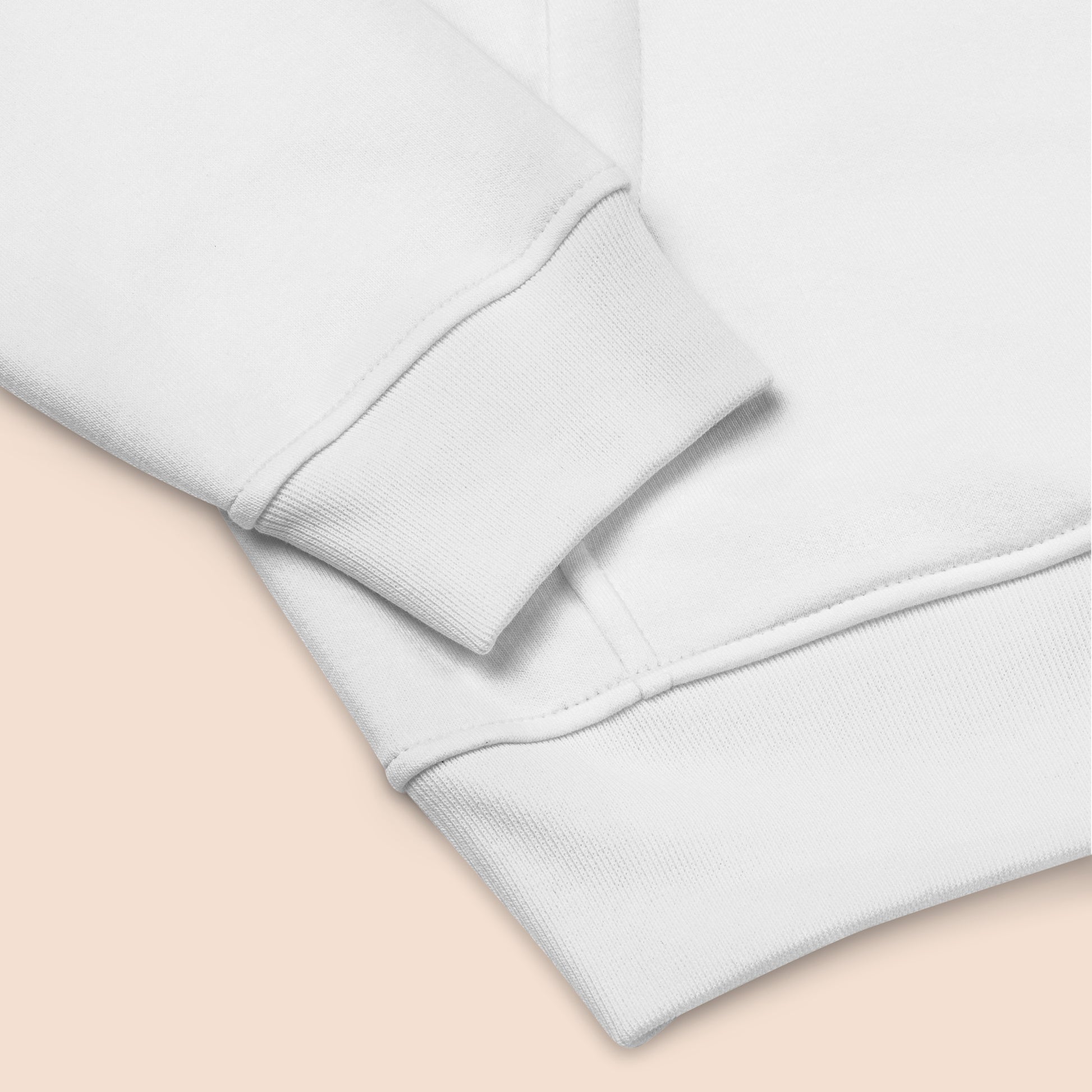 Close of of a white sweater sleeve and hem on a peachy beige background.