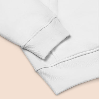 Close of of a white sweater sleeve and hem on a peachy beige background.