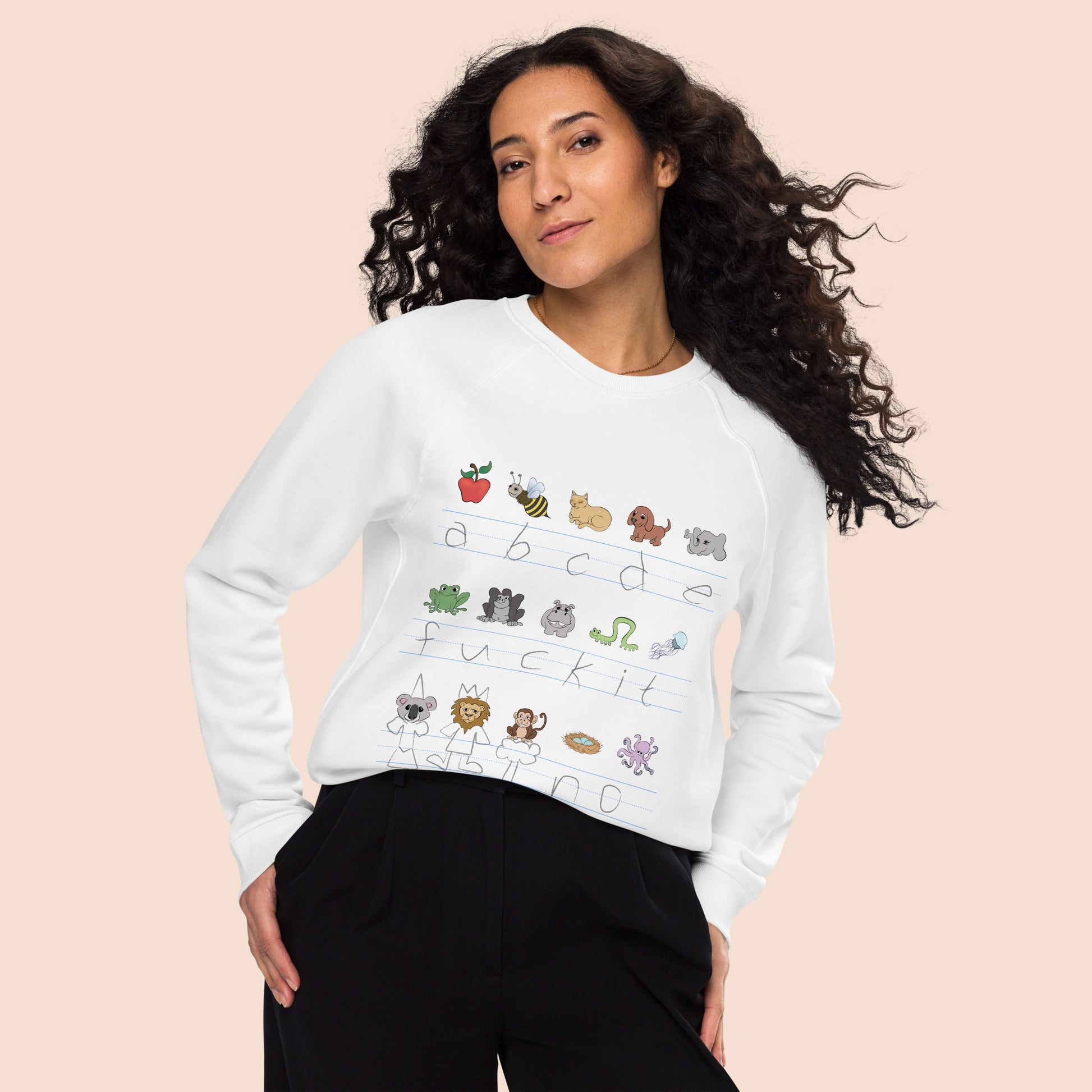 Woman with flowing black hair wearing a white sweatshirt with handwritten alphabet text (featuring a surprise) and colourful animal illustrations on a peachy beige background