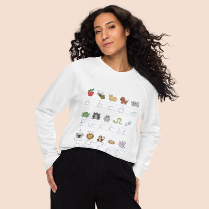 Woman with flowing black hair wearing a white sweatshirt with handwritten alphabet text (featuring a surprise) and colourful animal illustrations on a peachy beige background