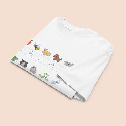 White t-shirt with cartoon animal illustrations and part of an alphabet on a peachy beige background