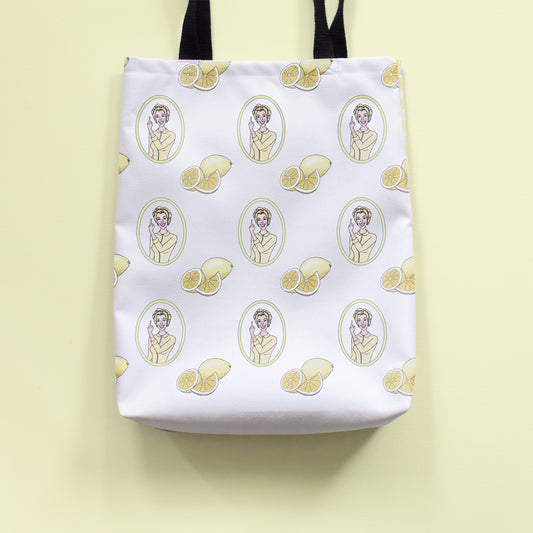 Tote bag with illustrated repeating pattern of a 1950s woman giving the middle finger inside an oval border, with lemon slices in between. The tote sits on a light yellow background.