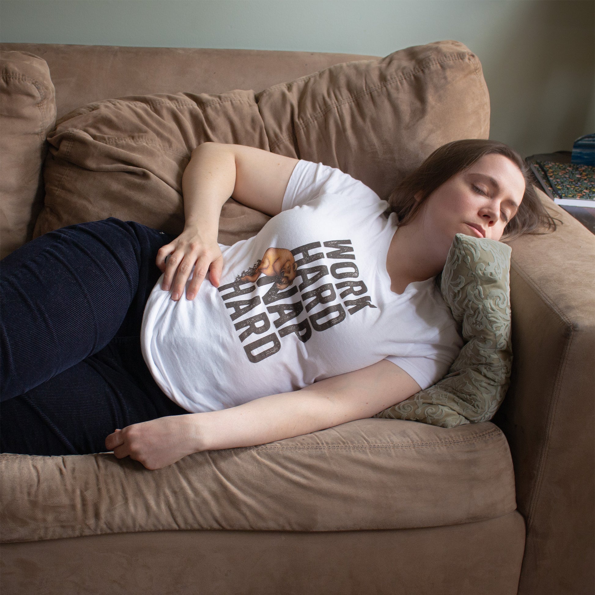 Woman wearing a shirt with a graphic of a sleepy bear and the text 'WORK HARD NAP HARD' while sleeping on a couch